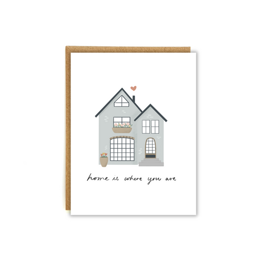 Cozy house illustration with a small heart coming out of the chimney. Featuring the phrase "home is where you are"